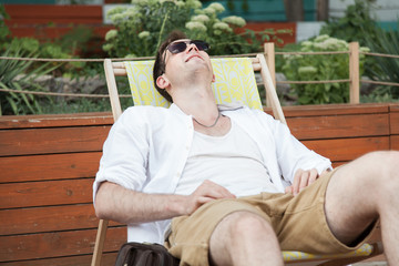  A young guy is sitting resting on a deckchair in the fresh air. Portrait.