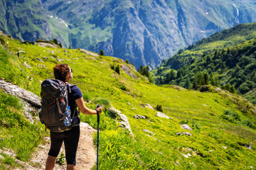 Female traveler with backpack hiking mountain trail and admiring views of Swiss Alps in Val de...