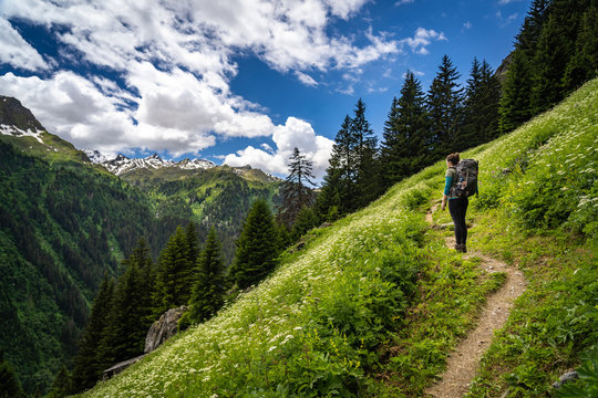Female traveler with backpack hiking mountain trail and admiring views of Swiss Alps in Val de Bagnes area, Switzerland.