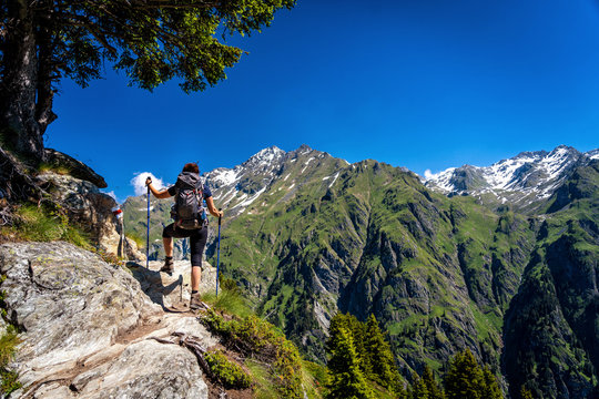 Female traveler with backpack hiking mountain trail and admiring views of Swiss Alps in Val de Bagnes area, Switzerland.