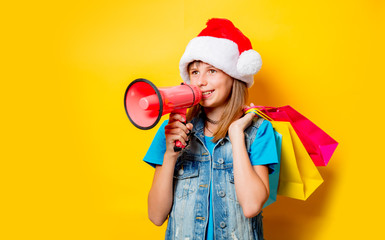 portrait of young teenage girl in Christmas hat with shopping bags and megaphone on yellow background