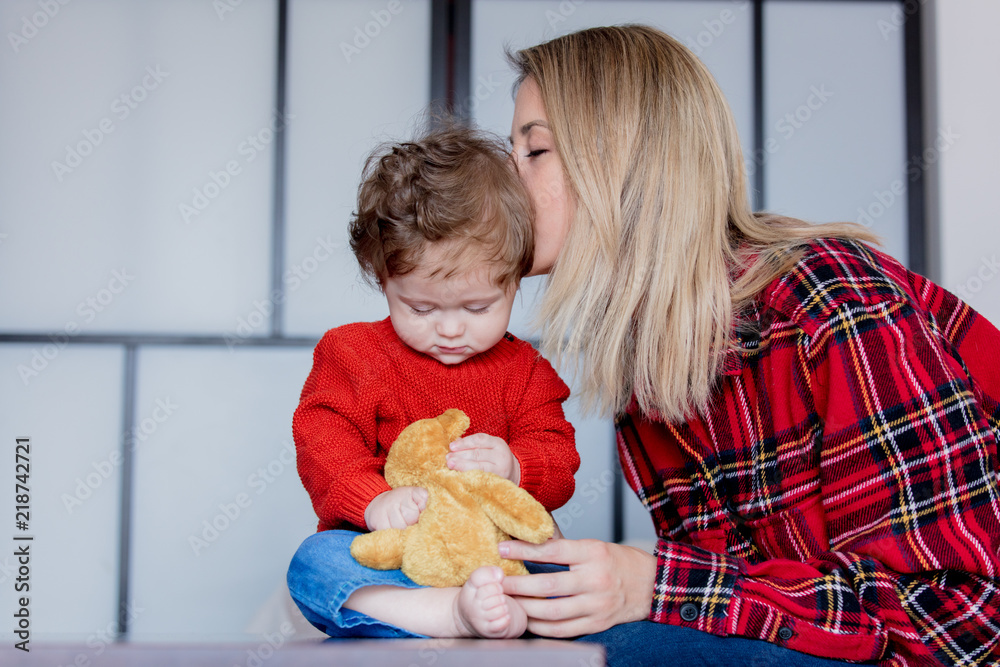 Wall mural mother and toddler baby play with teddy bead at home. red clothes, autumn season