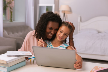 Caring mother. Positive delighted woman hugging her daughter while helping her with studying