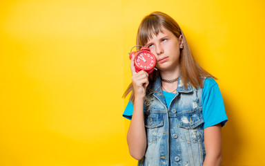 portrait of young teenage girl with alarm clock on yellow background