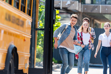 group of happy teen scholars running to school bus after lessons to get home