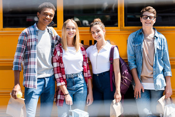 Group of teen happy scholars looking at camera while standing in front of school bus