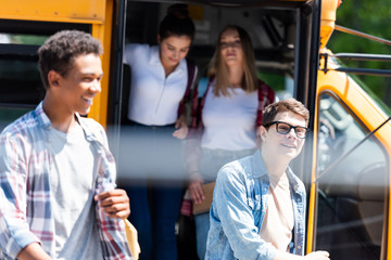 group of teen happy students walking out of school bus
