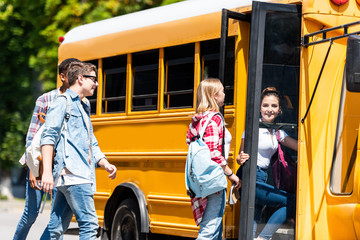 group of happy teen scholars entering school bus after lessons