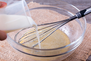 Mixing dough on kitchen table background with cooking ingredients ad add milk
