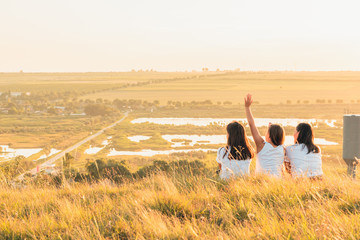 Group of three girls enjoying the sunset on a hill at countryside
