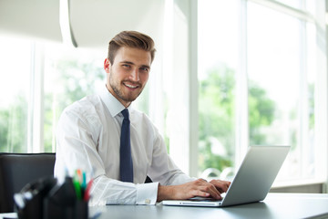 Happy young businessman using laptop at his office desk