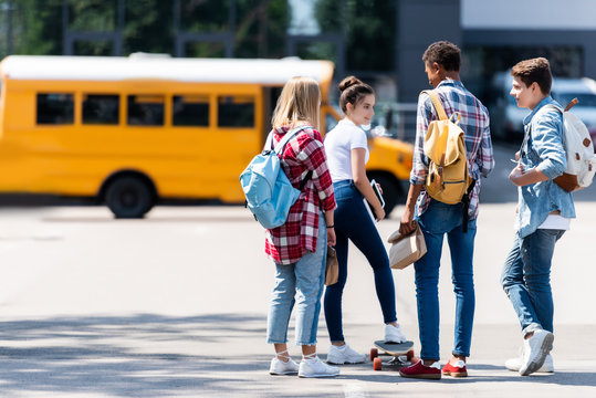 Group of teen scholars spending time together on parking in front of school bus
