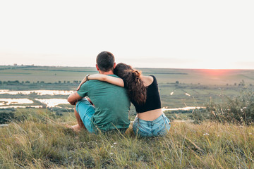Couple is hugging and sitting close on a hill at sunset