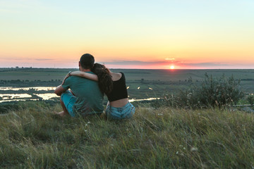 Couple is hugging and sitting close on a hill at sunset