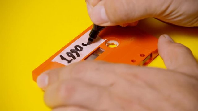 Writing the text 1990s on the rough label of a vintage cassette tape (obsolete music technology). Colorful scene.
