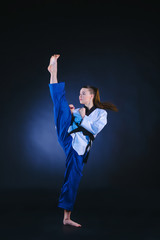 The karate girl in white kimono and black belt training karate over gray background. © master1305