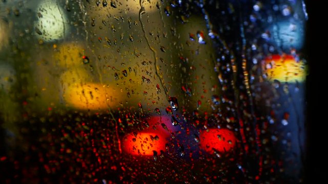 The concept of transportation on the night autumn city road in heavy raining, view inside the car moving on avenue. Automobile window in rain drops. Abstract blurred background with colorful lights