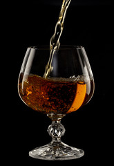 Cognac is poured into a glass, a spray of a drink, on a black background