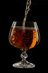 Cognac is poured into a glass, a spray of a drink, on a black background
