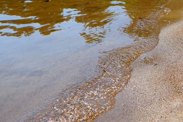 Close up of small wave on sandy beach.