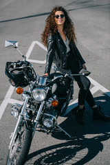 Fototapeta na wymiar happy female biker sitting on classic motorcycle on urban parking