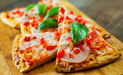 sliced Pizza with Mozzarella cheese, Ham, Tomatoes, pepper, Spices and Fresh Basil. Italian pizza on wooden background.