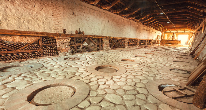 Huge stone cellar with aged dust wine bottles and qvevri, large earthenware vessels under ground. Rustic farmhouse interior with rural storage of winery.