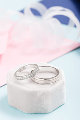 Two silver wedding rings with diamonds on pink background