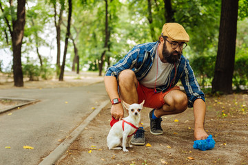Obraz premium Man in glasses. Bearded stylish man wearing black glasses taking care of his dog walking in the park