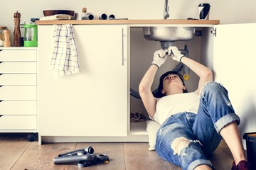 Woman fixing leakage sink in kitchen - obrazy, fototapety, plakaty