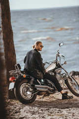 Fototapeta na wymiar biker in black leather jacket sitting on classical chopper motorcycle near the sea