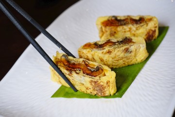 Use chopstick to pick up Japanese egg rolls with Grilled Eel (Unagi) on white plate