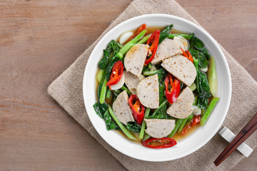top view of stir fried chinese kale and vietnamese pork sausage with soy sauce in a ceramic dish on wooden table. asian homemade style food concept.
