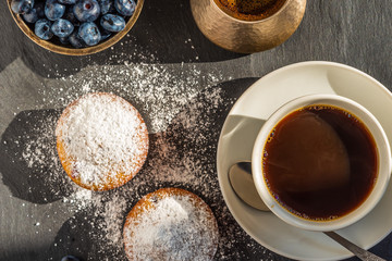 Delicious breakfast - a cup of coffee and muffins with blueberries on a slate platter