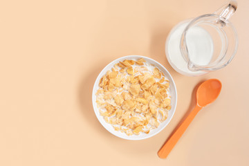 corn flakes in a bowl with jug of milk and plastic spoon on orange background, copy space for text. quick breakfast for modern lifestyle concept.