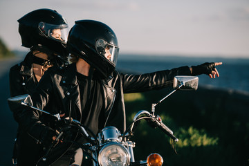bikers in helmets on motorcycle, man showing something to girlfriend