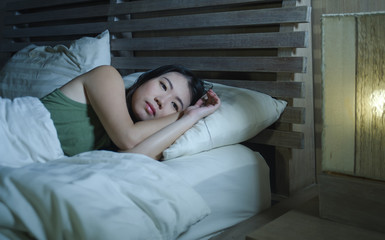 young beautiful depressed and sad Asian Chinese woman having insomnia lying in bed at night...