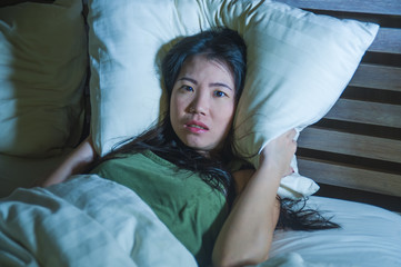 young beautiful scared Asian Chinese woman lying awake in bed sleepless covering head with pillow...