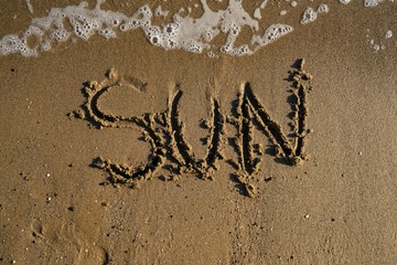 Word sun written on the sand washed by waves