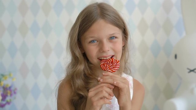 Funny child with candy lollipop, happy little girl eating lollipop, kid eat sweets at home