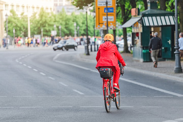 woman in red rides a bike at city street, view from the back