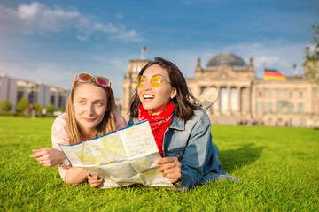Fototapeta premium Multiracial group of friends visiting the city of Berlin. Two women reading map with Reichstag building on the background. Friendship and travel concept with real candid emotions