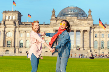 Naklejka premium Dwa młodej studenckiej dziewczyny ma zabawę, tana i piggybacking na trawie blisko sławnego punktu zwrotnego w Berlin - Bundestag budynek. Koncepcja podróży