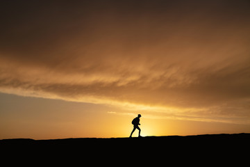 SIlhouette of a lonely woman walking at sunset on a hill