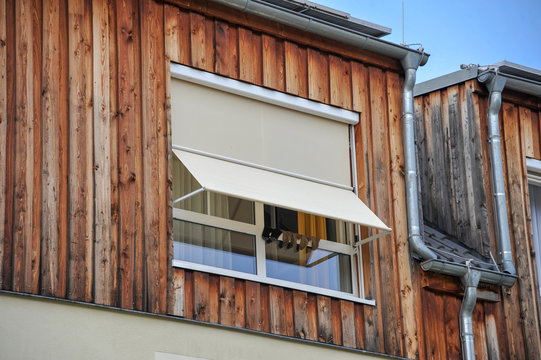 haus holzfassade holzverkleidung mit offenen Fenster und markise im sommer mit sonne und socken zum l&uuml;ften trocknen