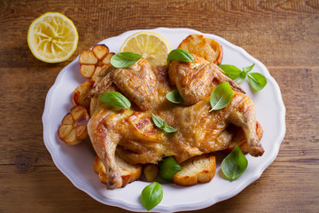 Whole chicken on toasted bread with lemon, basil and garlic on white plate, wooden table. horizontal