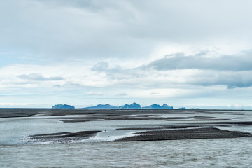 Landscape view of Heimaey island in south southern region in Iceland in distance from Seljalandsfoss, with river, cloudy stormy overcast sky, black sand near Vik