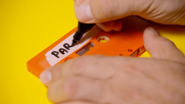 Writing the text Party Mix on the rough label of a vintage cassette tape (obsolete music technology). Colorful scene.
