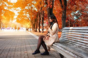 Woman enjoy autumn season sitting on bench in fall park and drinking coffee