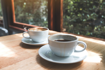 Closeup image of two white cups of hot coffee on wooden table in cafe